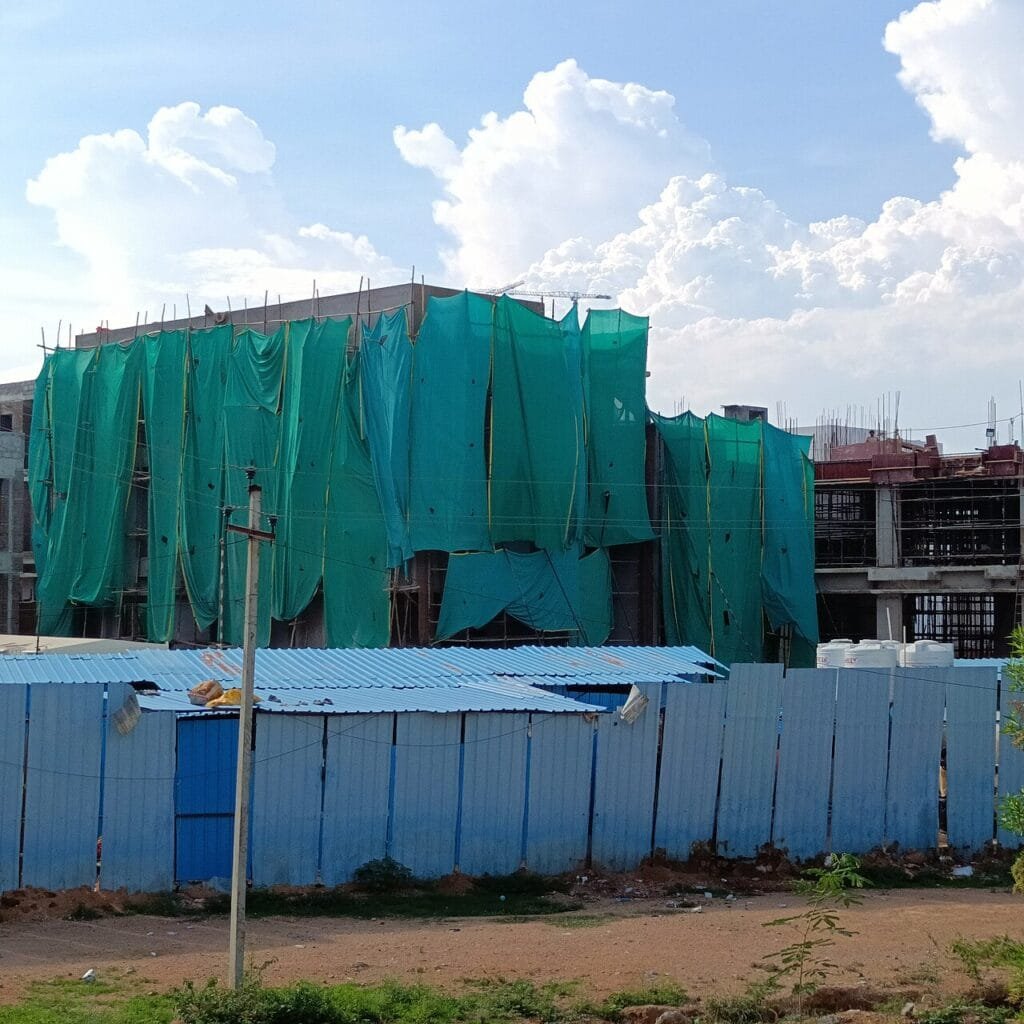 Multi-storey building under construction covered with green safety net behind a blue site boundary sheet